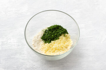 Glass bowl with semolina, grated cheese and chopped herbs on a light gray background. Cooking delicious homemade vegetarian food.
