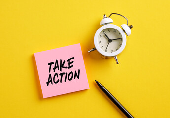 Take action message on pink note paper with alarm clock and pen. Motivational message for taking...