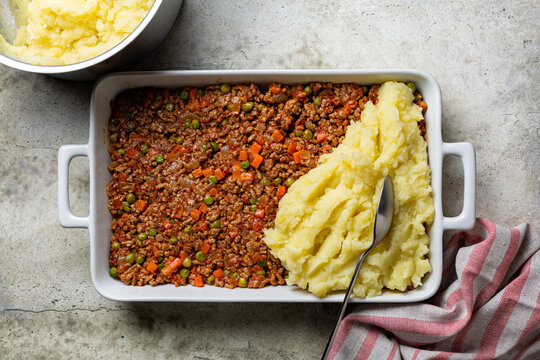 Process of cooking Shepherd's pie, or cottage pie, or French version hachis Parmentier. Cooked minced beef meat with vegetables topped with mashed potato, before baking.