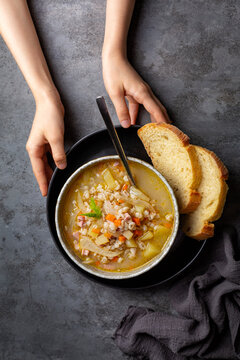 Hands holding homemade South Tyrolean barley soup Gerstsuppe, Graupensuppe, made with smoked pancetta or bacon, calery, fennel, potato, onion. Fresh bread.  Or Zuppa d'orzo.