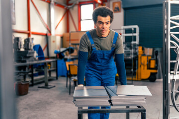 A worker in overalls and protective gloves stacks metal plates in a pile