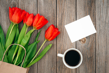 Bouquet of red tulips, a cup of coffee and a blank sheet, space for text.