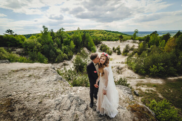 The bride and groom on the nature. Portrait of an attractive couple in country. Wedding ceremony near stony, rocky wall. Newlyweds getting married outdoors.