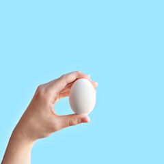 Fototapeta na wymiar Minimalist Easter greeting, advertising or promotion card design, white egg in a hand on blue background, food market mockup with copy space