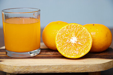 some oranges fruits and a glass of orange juice are served on a wooden table