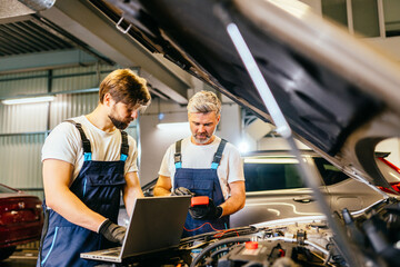 Team of two positive friendly car mechanics using a computer laptop to diagnosing and checking up...