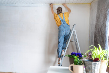 Young adult happy woman renovating the house, covering the walls with film before painting