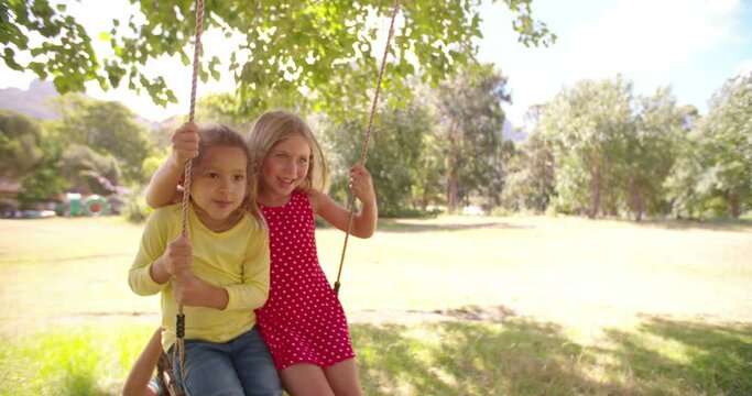 Childhood friends on a swing together happily in a park surrounded by nature, slow motion