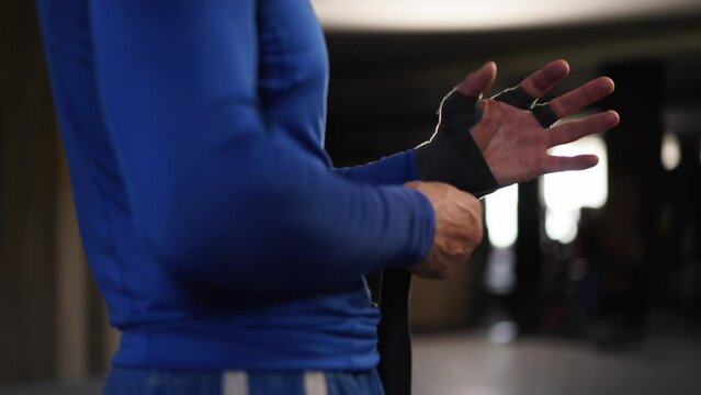 Athletic man wrapping hands with boxing bandages at gym. Male fighter wrapping his hands with black protection bandages. Male athlete preparing for fight in a gym. Sport, active lifestyle concept. 