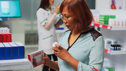 Female client looking at cardiology pills boxes to buy treatment, visiting medical store. Woman checking pharmaceutical products packages and bottles of drugs to cure disease. Handheld shot.
