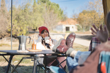 Couple having coffee outside their camper van - couple enjoying a day camping - Winter vacations and relationship concept.
