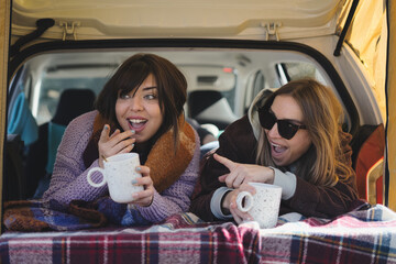 Couple lying inside the van with a cup of coffee - couple with surprised expression - Winter...