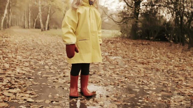 Girl with red rubber boots jumping into puddle