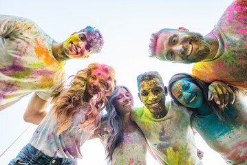 Multiethnic group of happy playful friends playing and having fun with holi colorful powder at the park