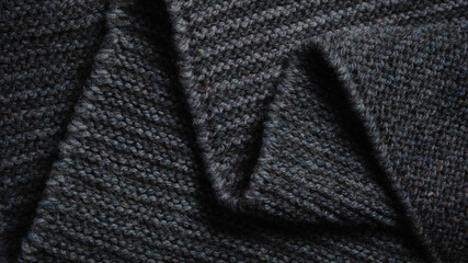 Black knitted fabric folded in a zigzag pattern. Knitted texture background.