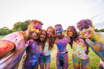 Multiethnic group of happy playful friends playing and having fun with holi colorful powder at the...