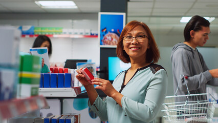 Female buyer looking at pharmaceutical products to find medicine, analyzing packages of medicaments on shelves. Woman searching for pills and supplements, pharmacy shop. Handheld shot.