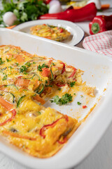 Oven baked frittata with mediterranean vegetables in a white baking dish on kitchen table.