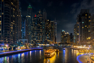 Fototapeta premium Dubai Marina cityscape at night with illuminated skyscrapers and boats in canal. UAE