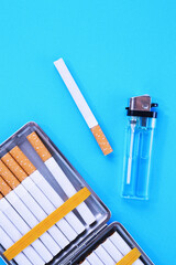 Cigarettes, case and lighter against pale blue