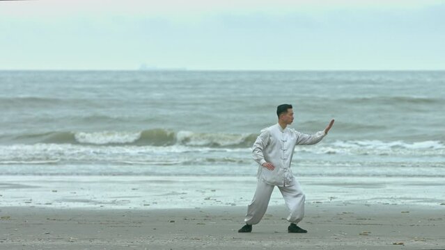 Chinese warrior in traditional kimono practicing kung-fu on beach.