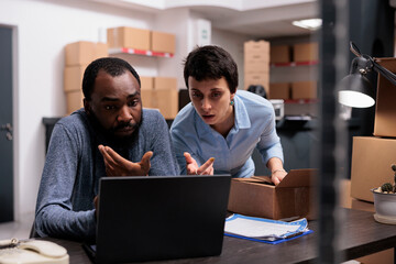 Diverse team looking at cargo stock on laptop computer discussing transporation logistics while working in warehouse delivery department. Employees planning new delivery packaging