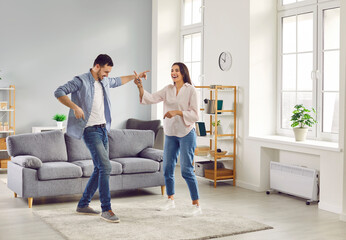 Happy overjoyed laughing young couple homeowners having fun dancing at home in living room...