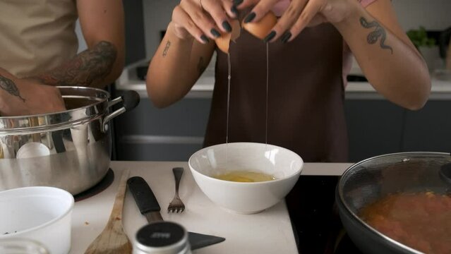 Young Venezuelan woman breaking eggs to prepare the filling for the arepas at kitchen.