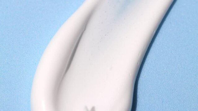 Smear of white cosmetic cream on a blue background. Texture of a skin care product close-up sample for make-up.