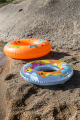 There are two inflatable swimming circles on the beach. y orange.