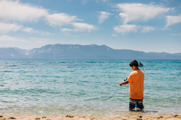 Kid Stands in a Mountain Lake with Blue Sky and Clouds