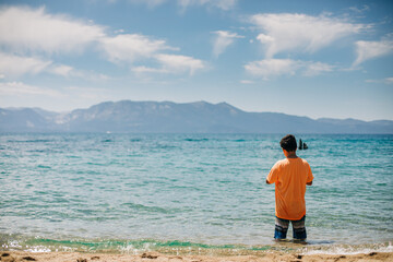 Fototapeta na wymiar Kid Stands in a Mountain Lake with Blue Sky and Clouds