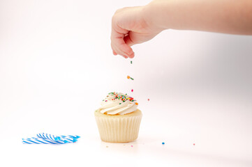 Child's hand decorating a cupcake with sprinkles and birthday candles