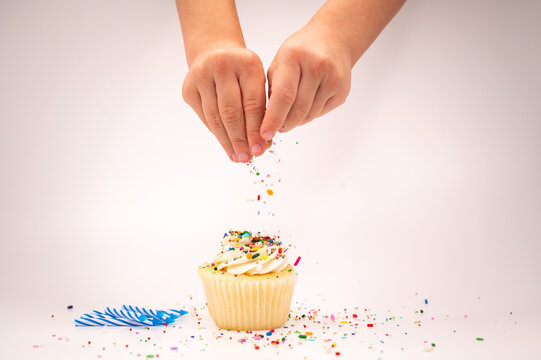 child's hand decorating birthday cupcake with sprinkles