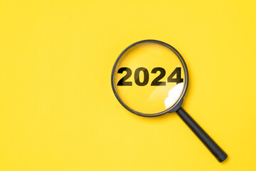 2024 year inside of magnifier glass on yellow background for focus and preparation new year change...
