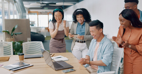 Fototapeta premium Winner, yes and applause with a business asian man cheering with his team while working on a laptop on his office. Goal, wow and success with a male employee and colleague group in celebration