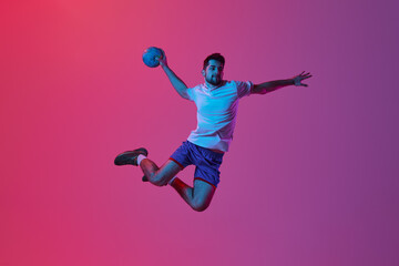 Fototapeta na wymiar Throwing ball in jump. Young man, professional handball player training, playing isolated on gradient pink background in neon light. Concept of sport, action, motion, championship, sportive lifestyle