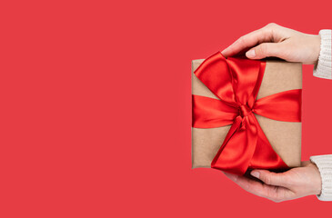Woman's hands hold gift box with red bow on red background. Banner. Close-up. Copy space. Top view. Selective focus.