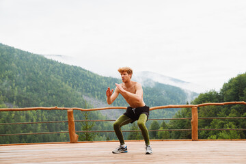 Athletic man in doing squat exercises during workout on in mountains