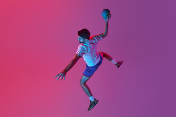 Obraz na płótnie Canvas Top view. In a jump. Young man, professional handball player training, playing isolated over gradient pink background in neon light. Winner. Concept of sport, action, championship, sportive lifestyle