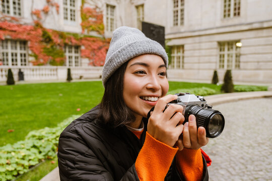Beautiful smiling asian woman taking pictures with vintage camera while sitting in old city