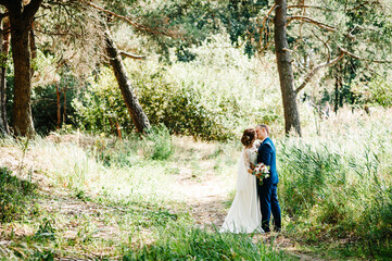 Bride and groom in a park kissing. Couple newlyweds in green forest are kissing, photo portrait. Wedding Couple in nature.