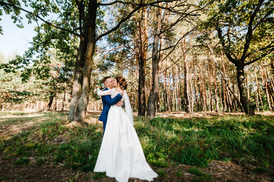 Bride and groom in a park kissing. Couple newlyweds in green forest are kissing, photo portrait. Wedding couple in nature.