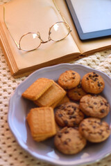 Plate of cookies, cup of tea, fresh blueberries, dry oranges, stack of books, reading glasses and tablet on the table. Hygge at home. Selective focus.