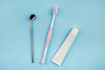 A set for oral care. Pink toothbrush, toothpaste and dental mirror on a blue background. The concept of dentistry and healthcare. Top view, flat position.  Copy space for text
