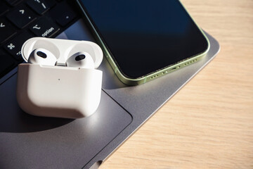White wireless bluetooth headphones with green smartphone on laptop on wooden background. High...