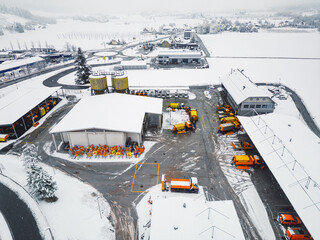 Aerial view of highway maintenance base, orange and yellow trucks and equipment stored on the base - Winter time