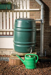 Green rain barrel and watering can to collect rain water, concept of water conservation
