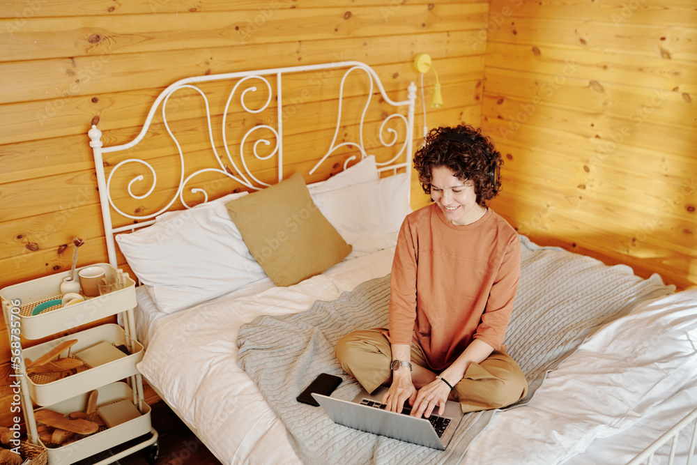 Aufkleber smiling female freelancer or student typing on laptop keypad while sitting on comfortable bed in spa