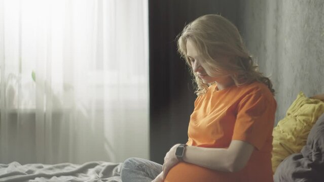 Happy pregnant woman resting on bed at home. The girl is stroking her baby's belly. The lifestyle of the emergence of a new life. High quality 4k footage